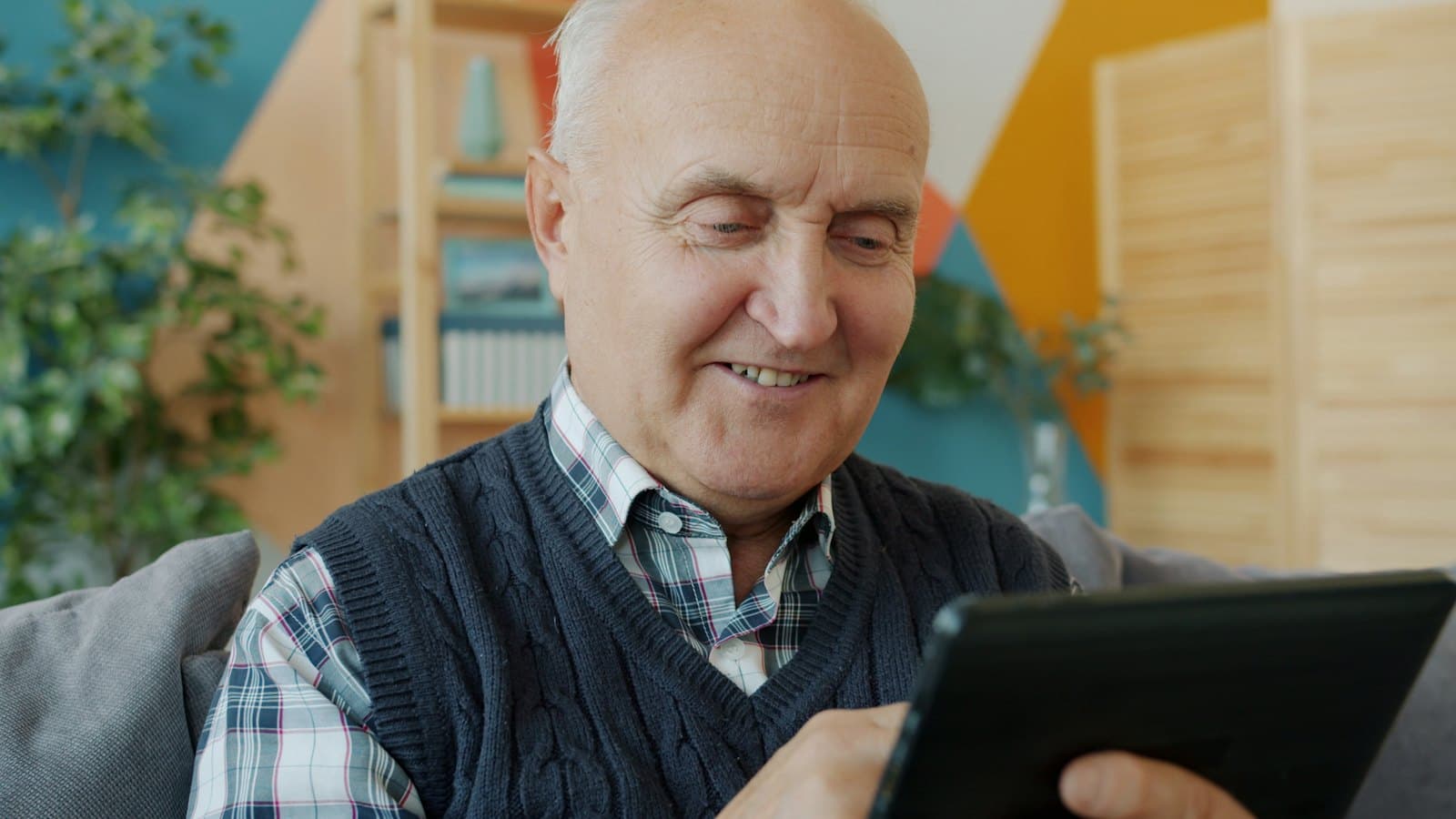 An older man smiling while using a tablet at home