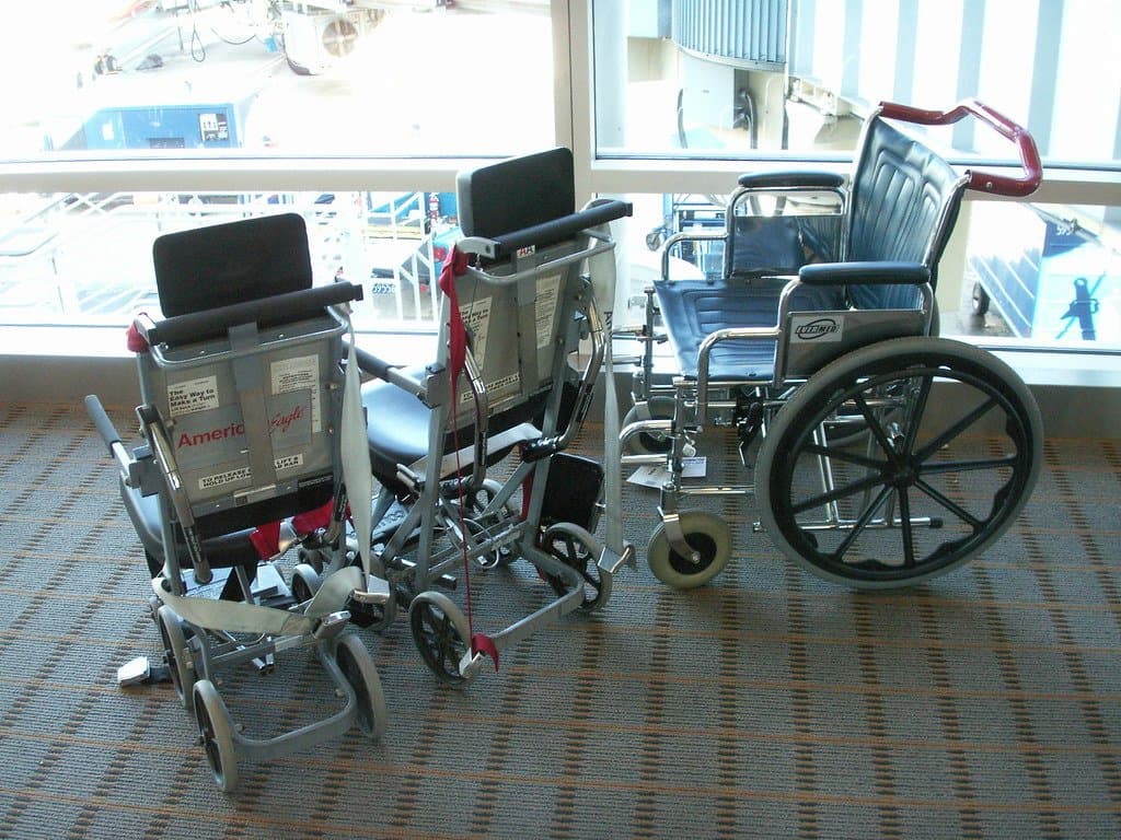 Two narrow airline aisle chairs and a standard wheelchair waiting at an airport gate