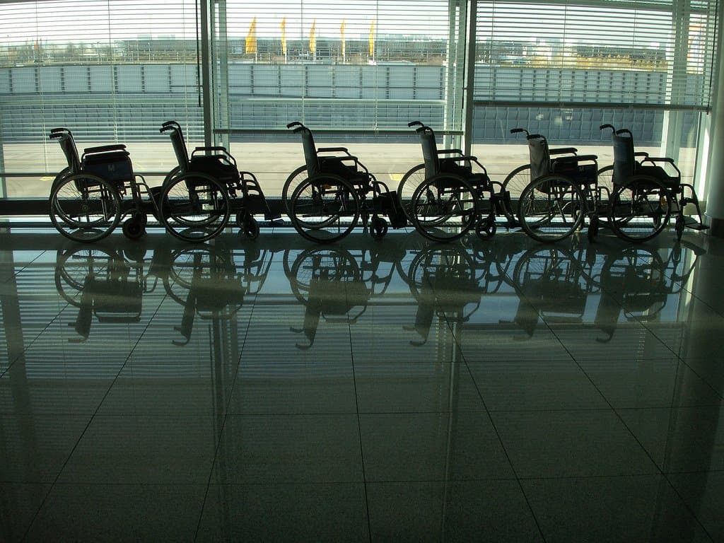 A row of airport wheelchairs lined up along a terminal window