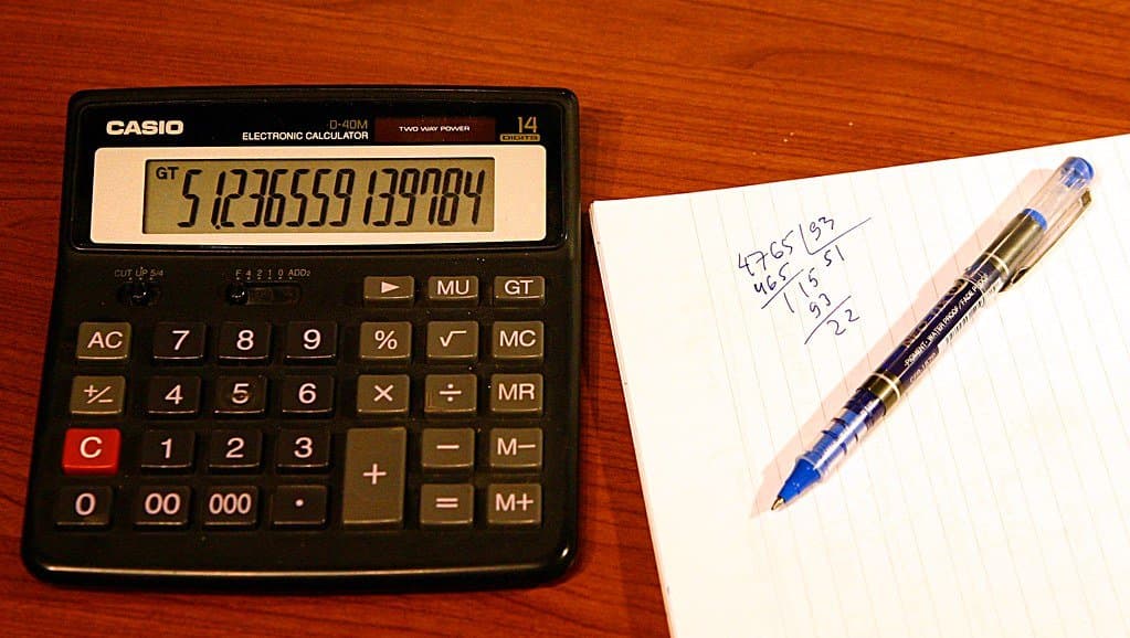 A calculator beside a notepad with handwritten figures and a pen