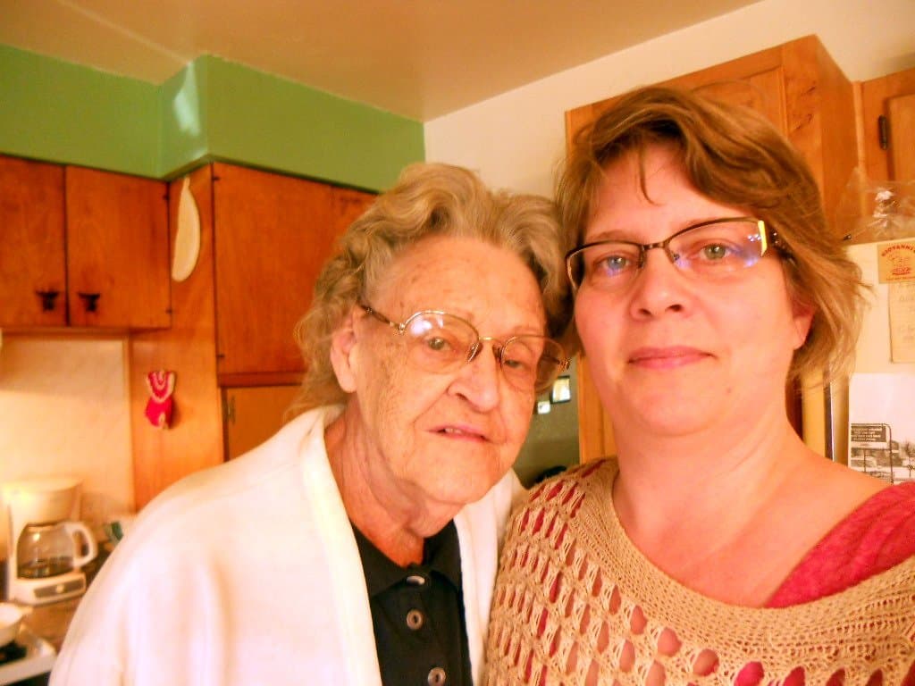 An adult daughter and her older mother side by side in a home kitchen