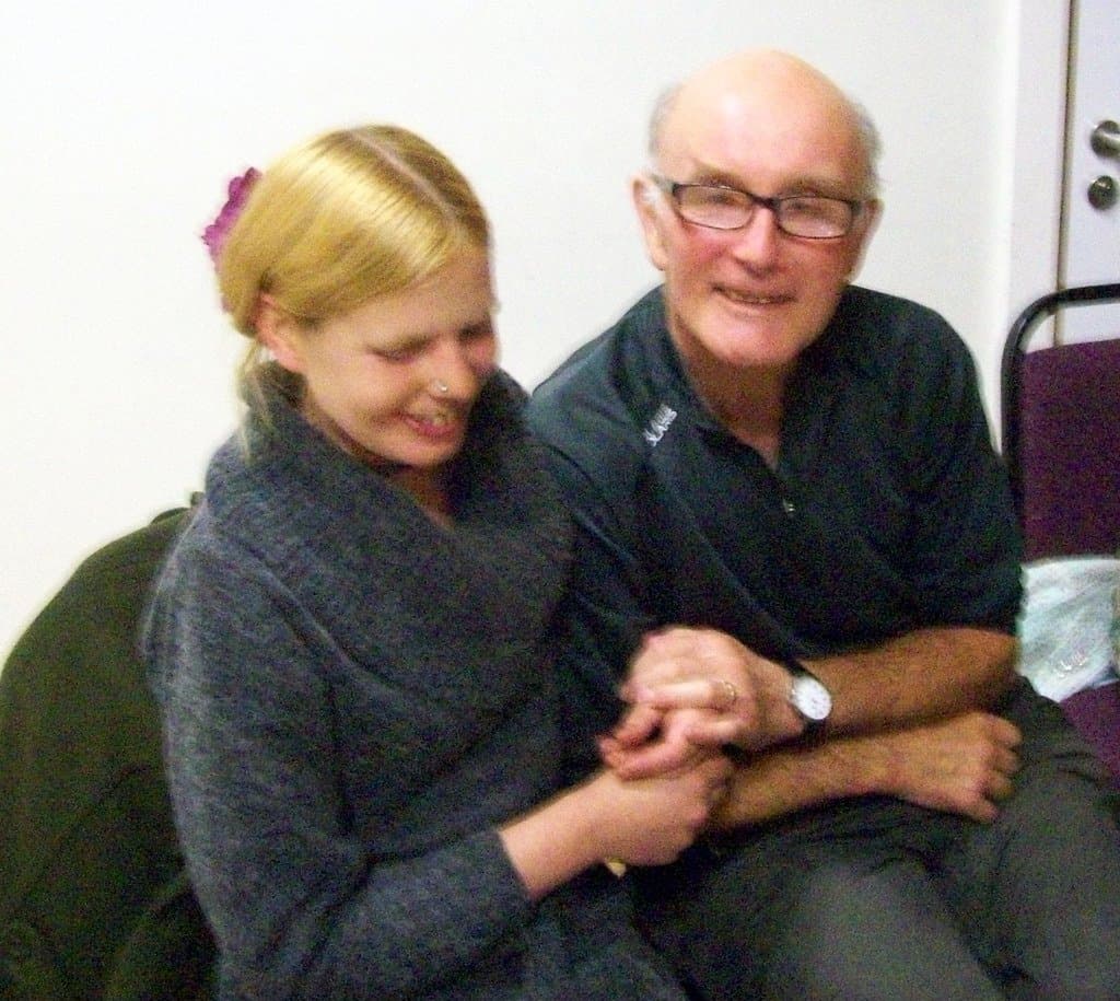 A younger woman holding hands with a smiling older man as they sit together