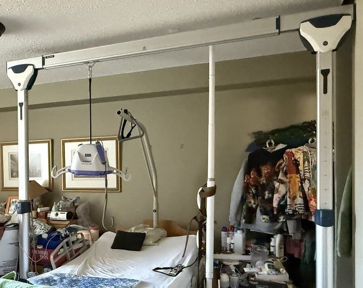 A freestanding ceiling-style track lift set up over a hospital bed in a bedroom at home