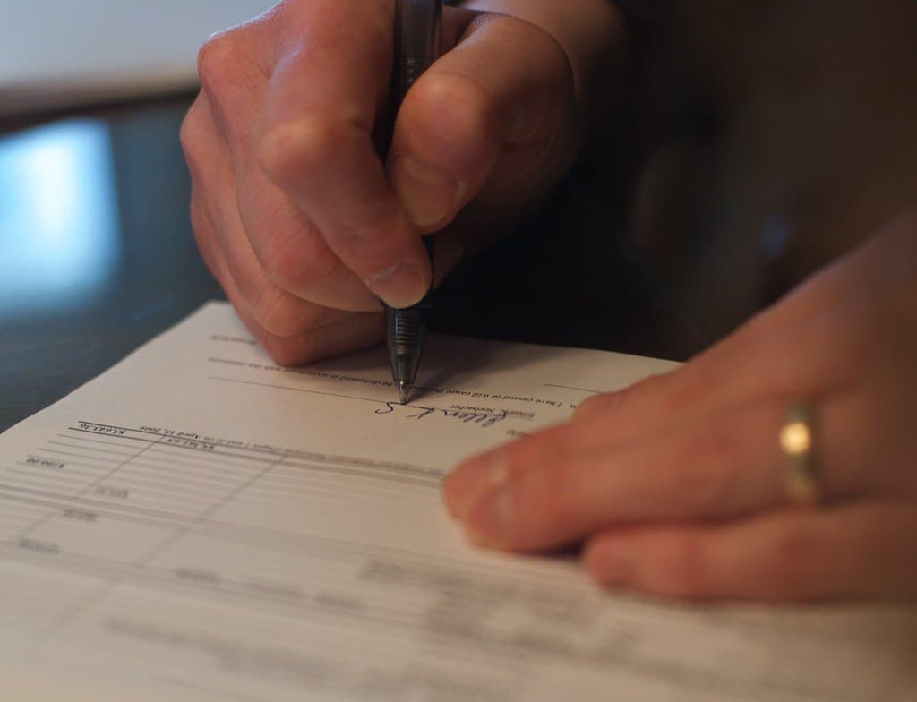 A hand wearing a ring signing a printed legal form with a pen
