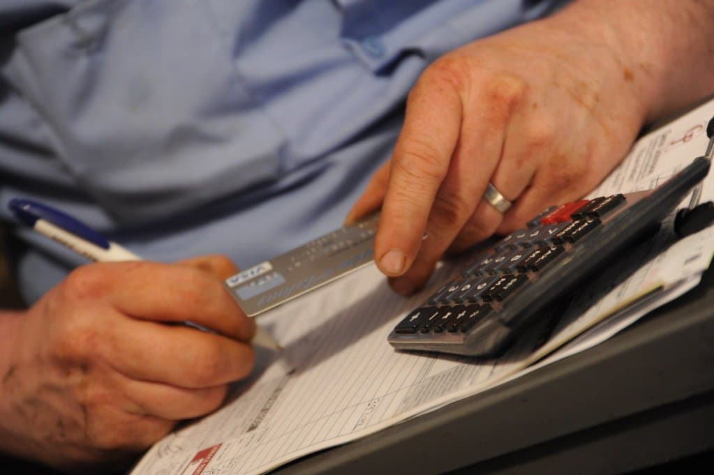 A man's hands holding a calculator and a pen over a bill, working out the charges