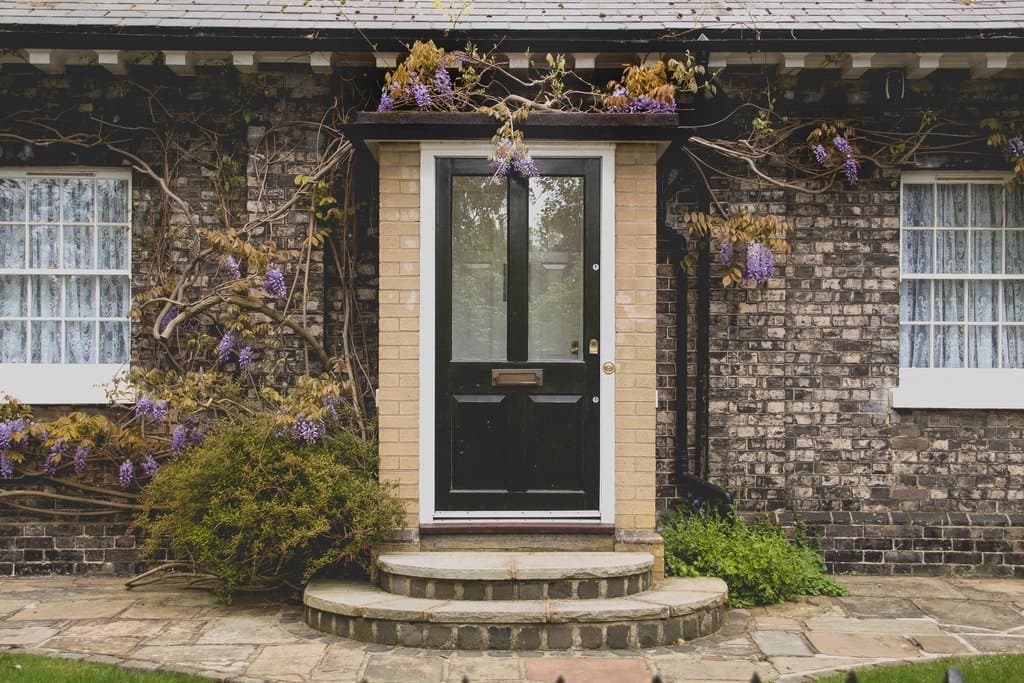 The front door of a brick house with wisteria in bloom over the entrance