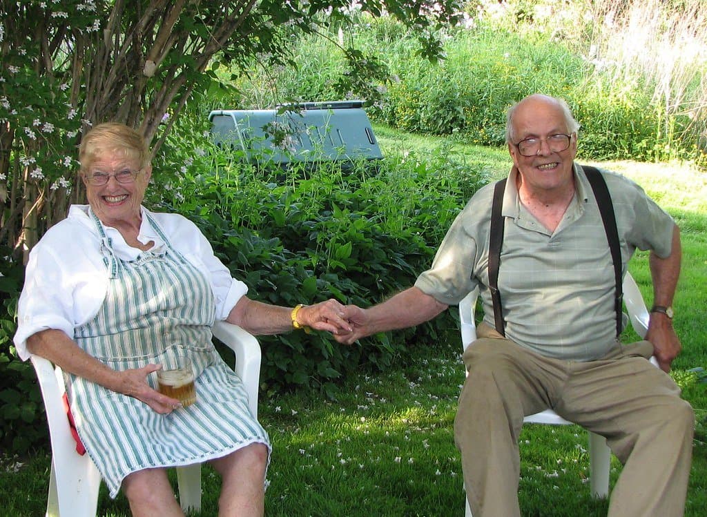 An older couple sitting in garden chairs, smiling and holding hands
