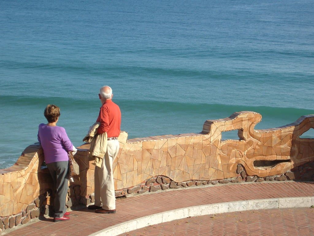 An older couple standing at a seaside wall, looking out over the ocean
