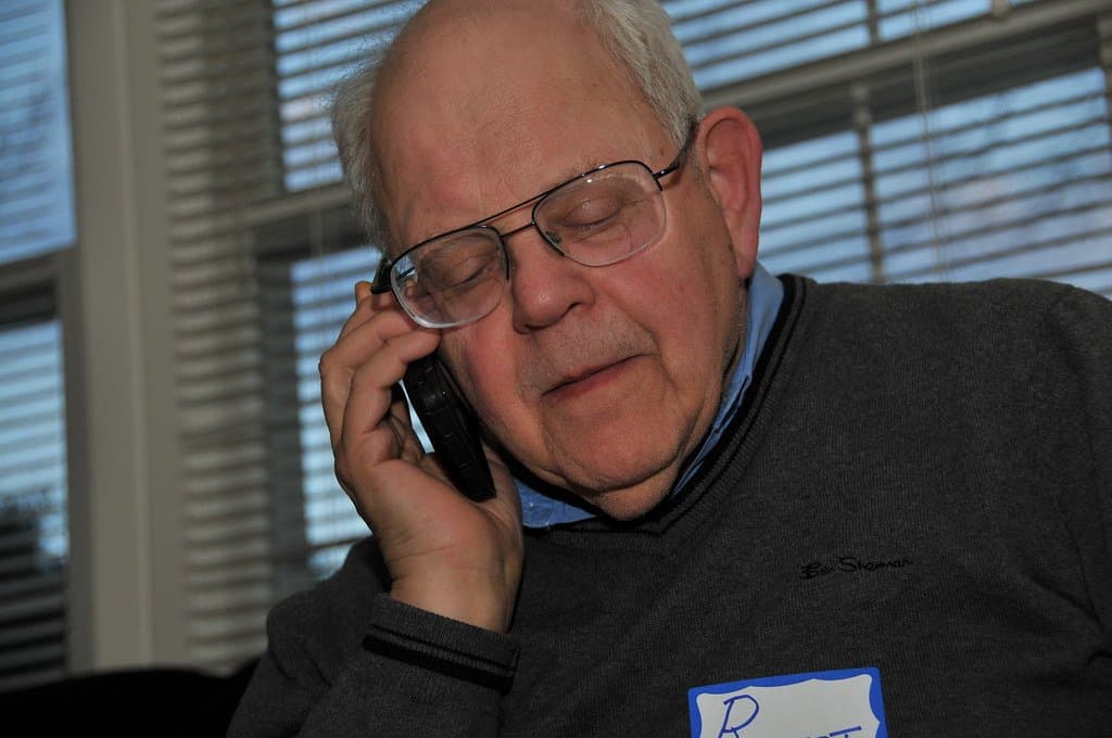 An older man with glasses listening closely on a mobile phone, looking concerned