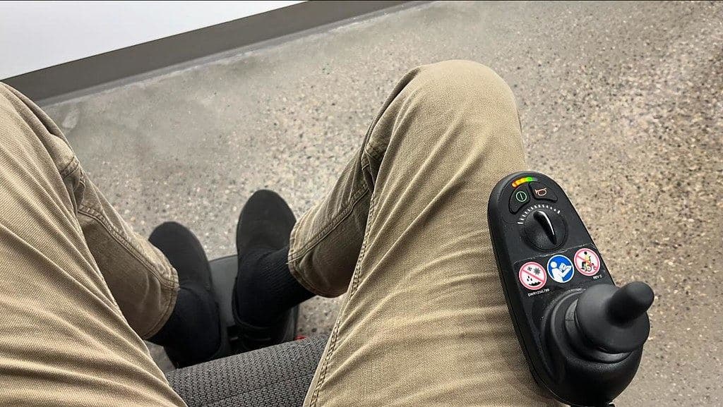 The view from a power wheelchair seat, with the joystick control on the armrest