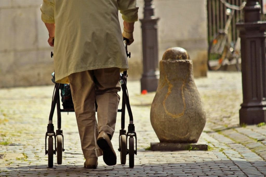 An older man walking down a cobblestone street with a four-wheeled rollator