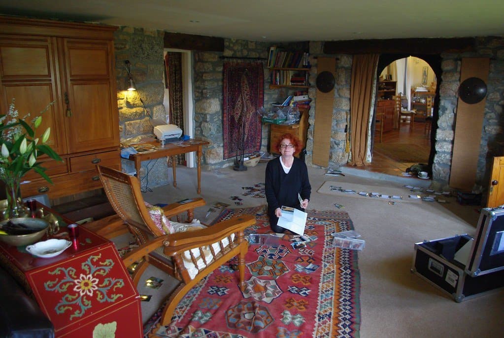 A woman kneeling on a rug in a living room, sorting through old family photographs and papers