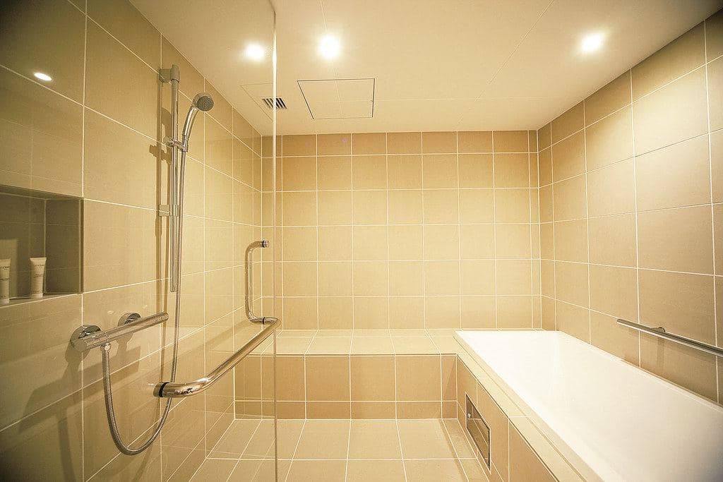 A step-free walk-in shower with a hand-held shower head, grab bars and a low bathing bench